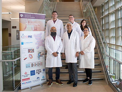 Dr. Balakrishna Haridas and lab personnel on the steps of the Emerging Technologies Building with an SWPDC informational banner.