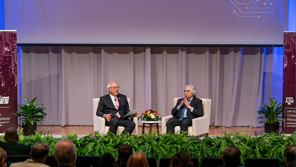 Left to right: Ray Rothrock and Ernest Moniz sit on chairs on stage at the Global Cyber Research Institute Summit in front of an audience. 