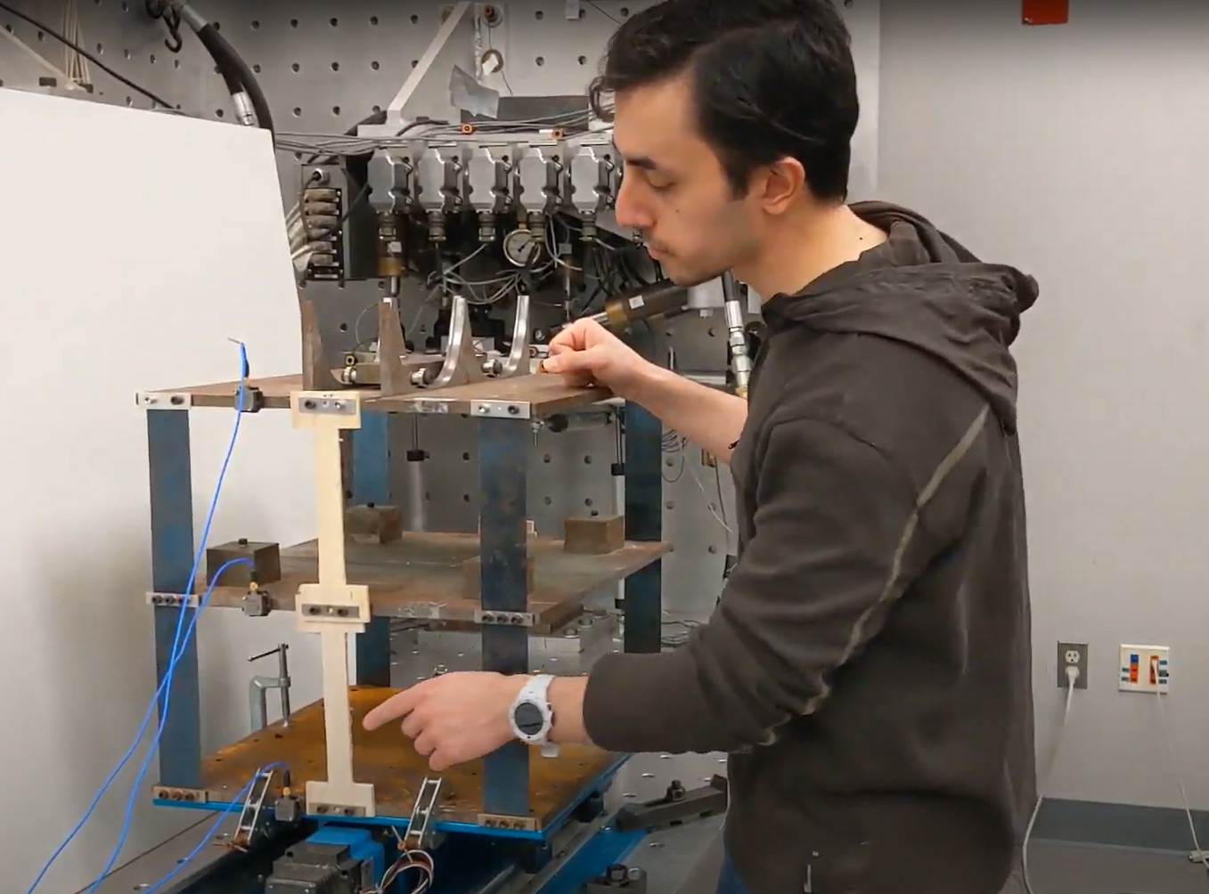 Najafi sets up a scaled model of a two-story steel structure on a shake table. The model has multiple sensors and wires attached to it.