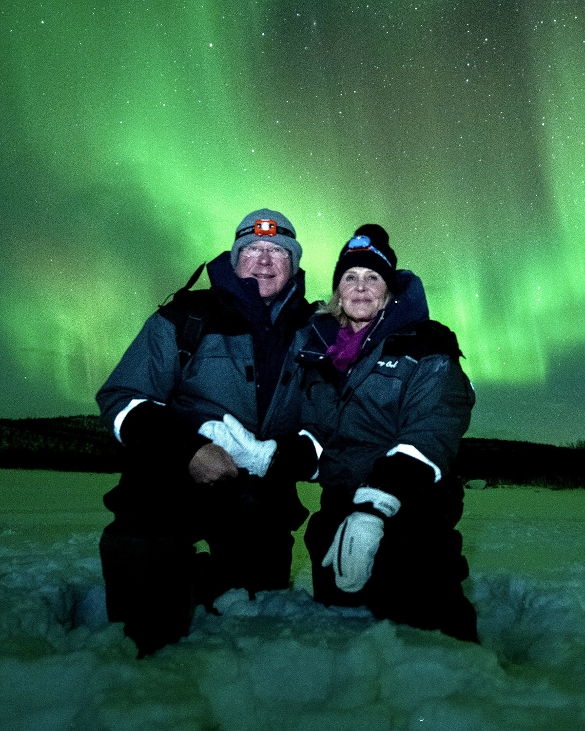 Susan and James F. "Jim" Thompson ’83, kneeling in the snow with the Northern Lights behind them.