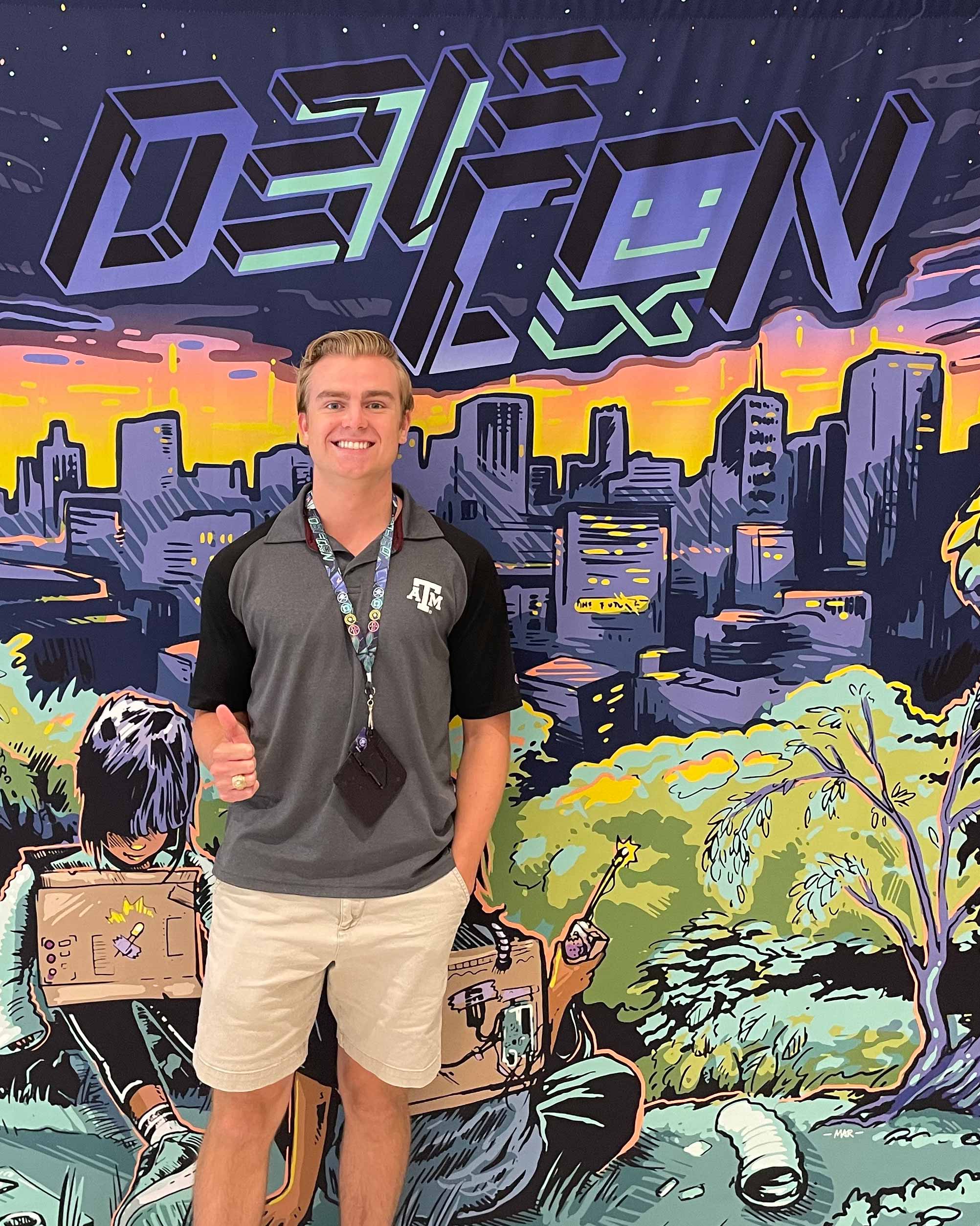 Connor McLaren stands in front of a colorful mural for DEF CON. 