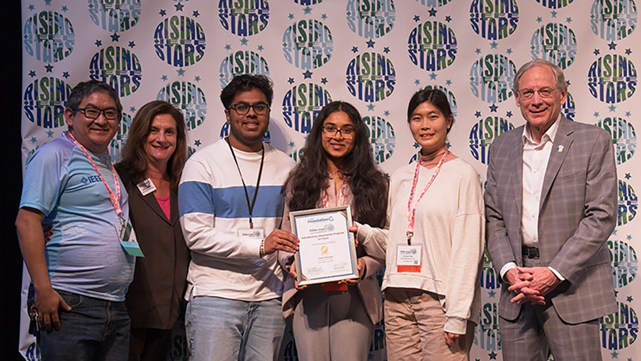 Karthik Ravikumar, Deeptha Karur and Christin Park, receive the first-place award from Scott Tamashiro, Eileen Russ Heltzer, and John D. McDonald in front of a banner that reads "rising stars" over and over again.