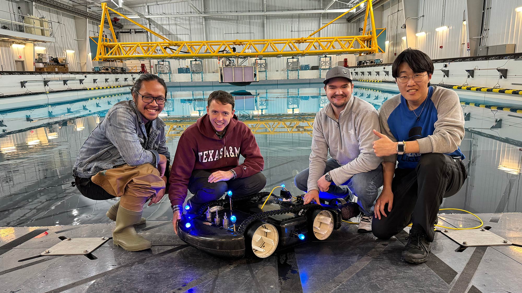 Four male students kneeling down in front of a four-wheeled robot.