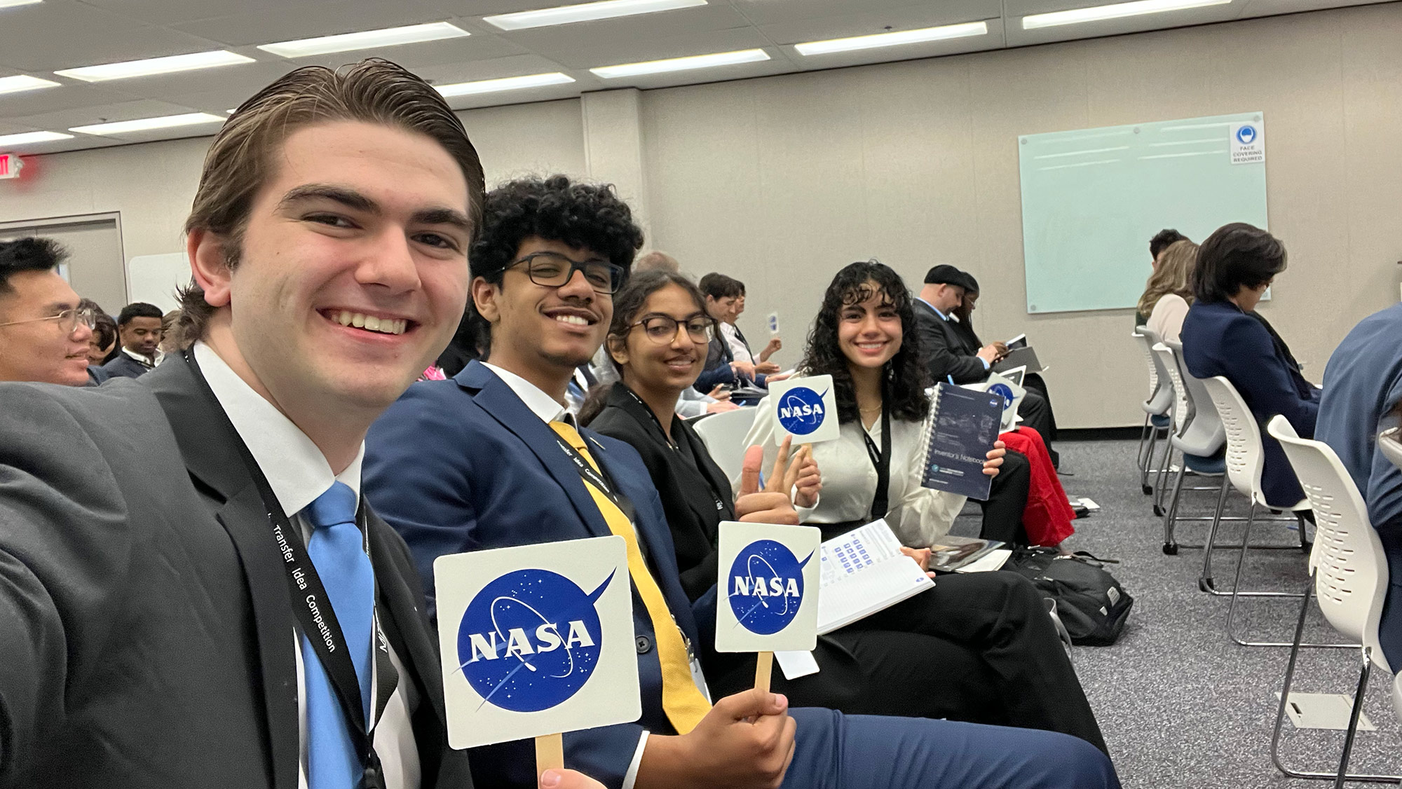 A group of students sitting in a conference room and holding up NASA signs.