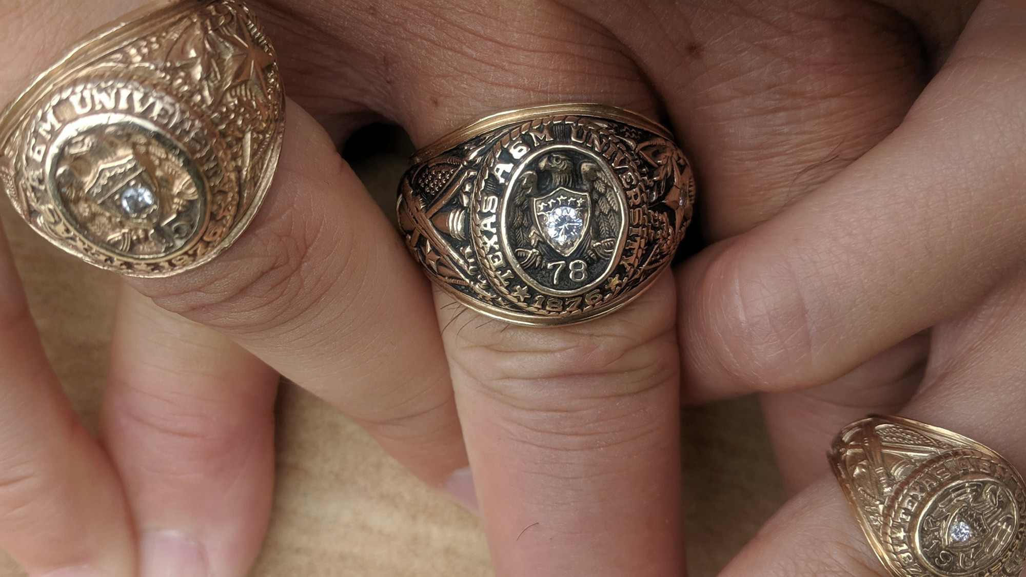 Three hands showing their Aggie Rings.