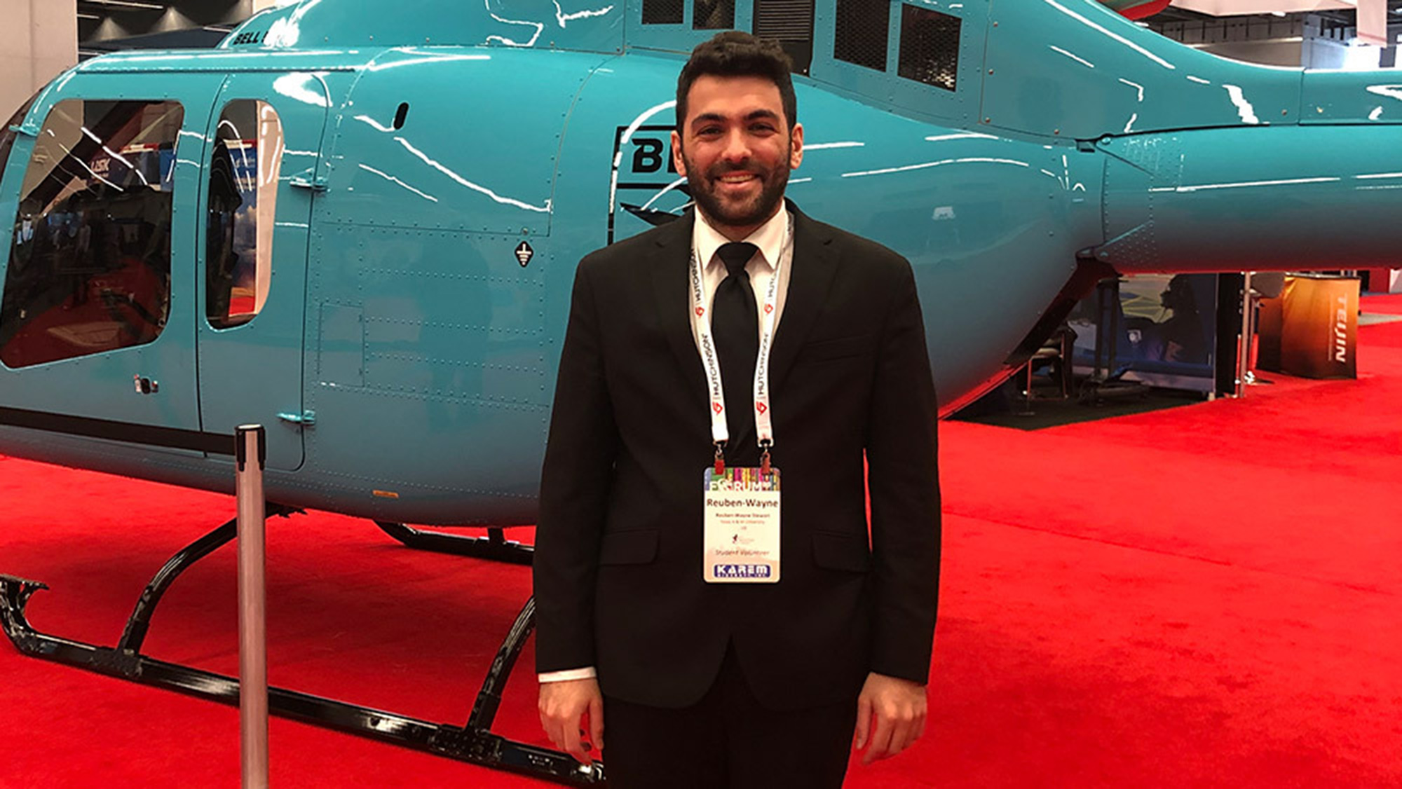 Man in suit standing in front of blue helicopter.