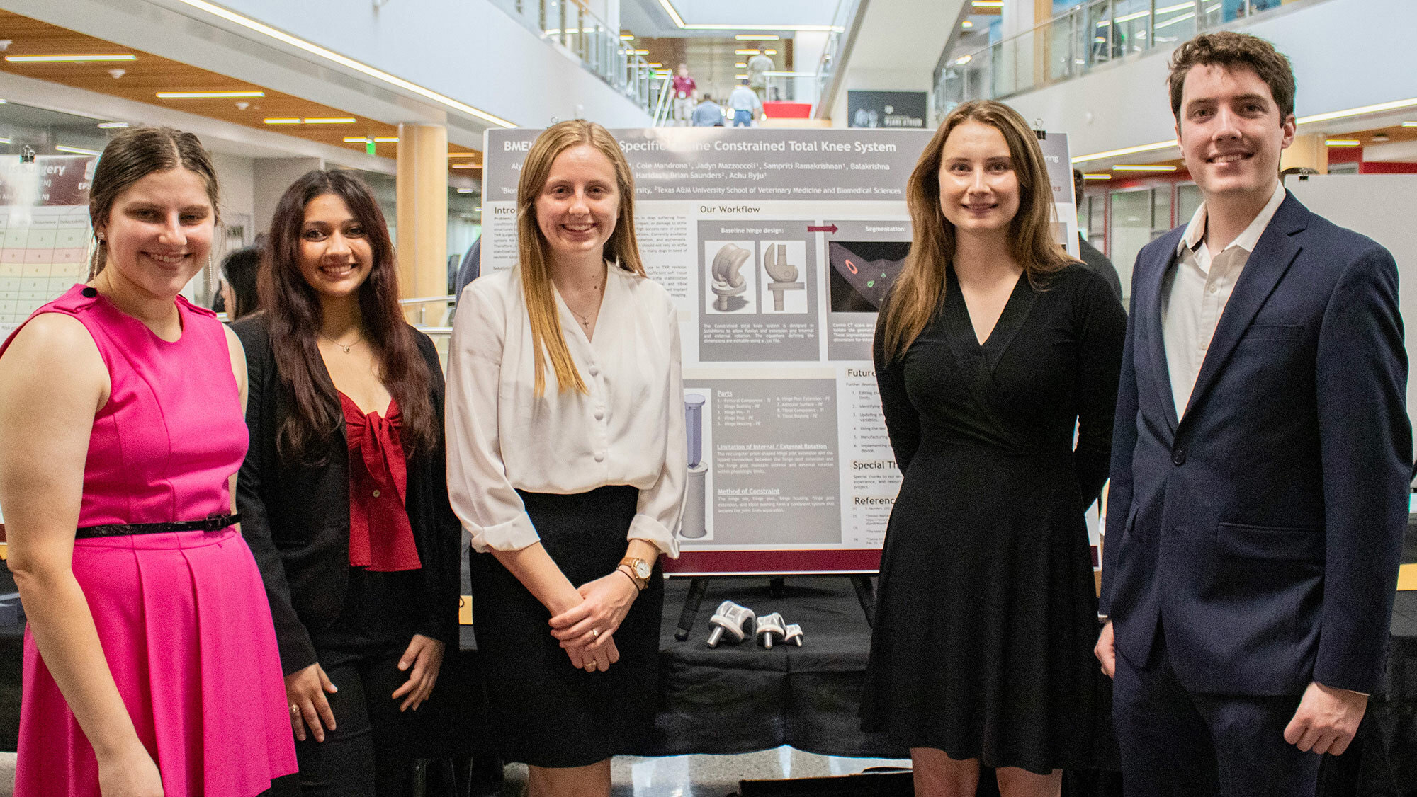 Five students standing in front of their poster presentation dressed in business casual.