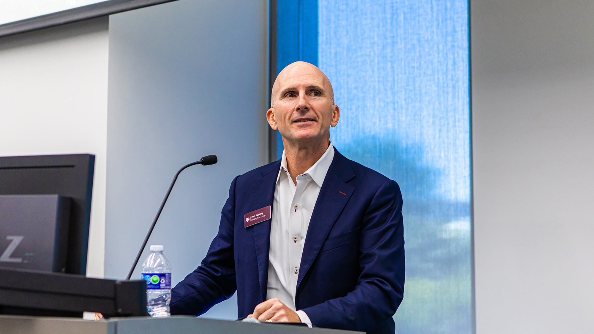 A man standing behind a lectern speaks into a microphone while gesturing.