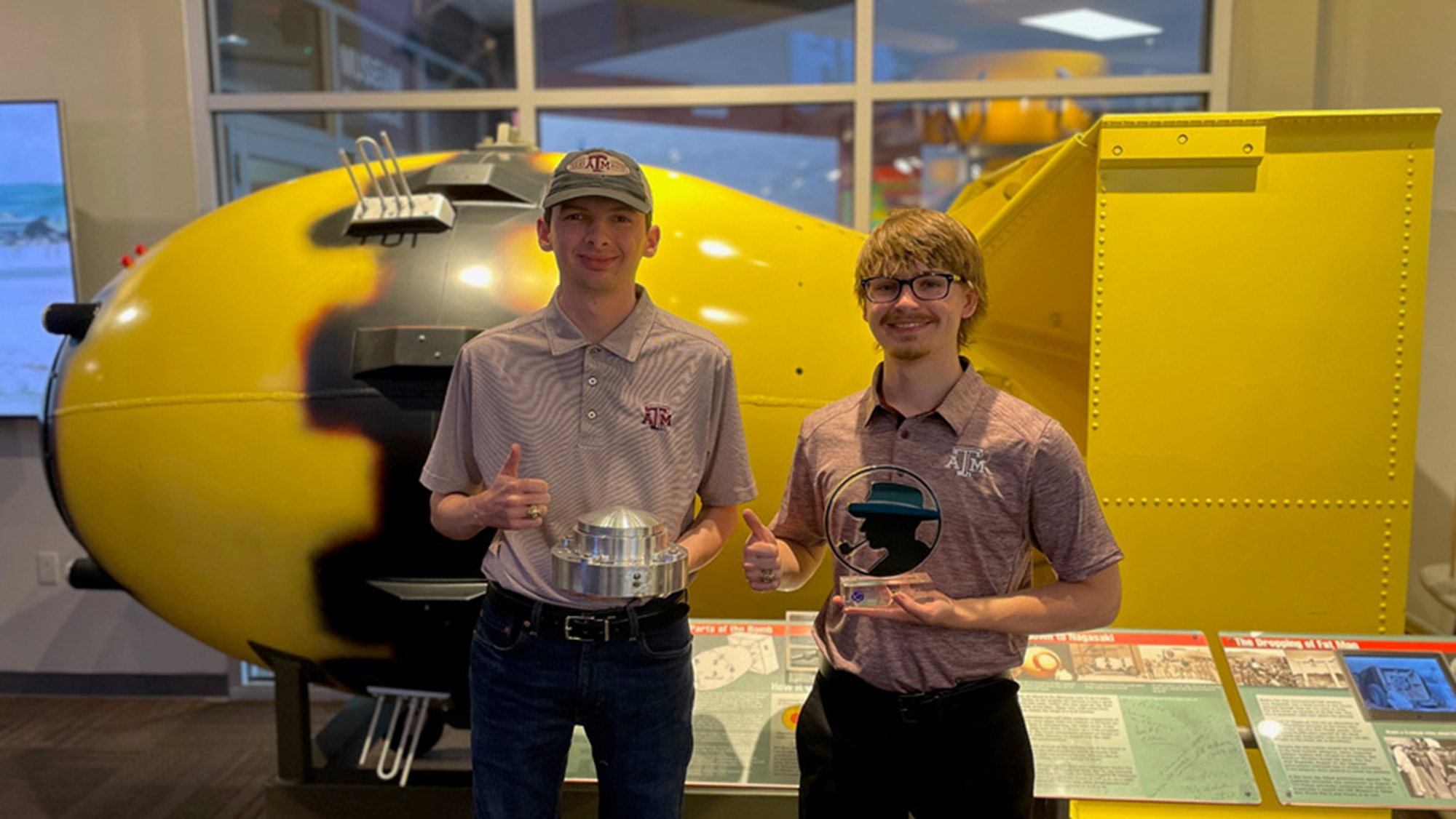 Two young men smiling and holding awards while giving thumbs up.