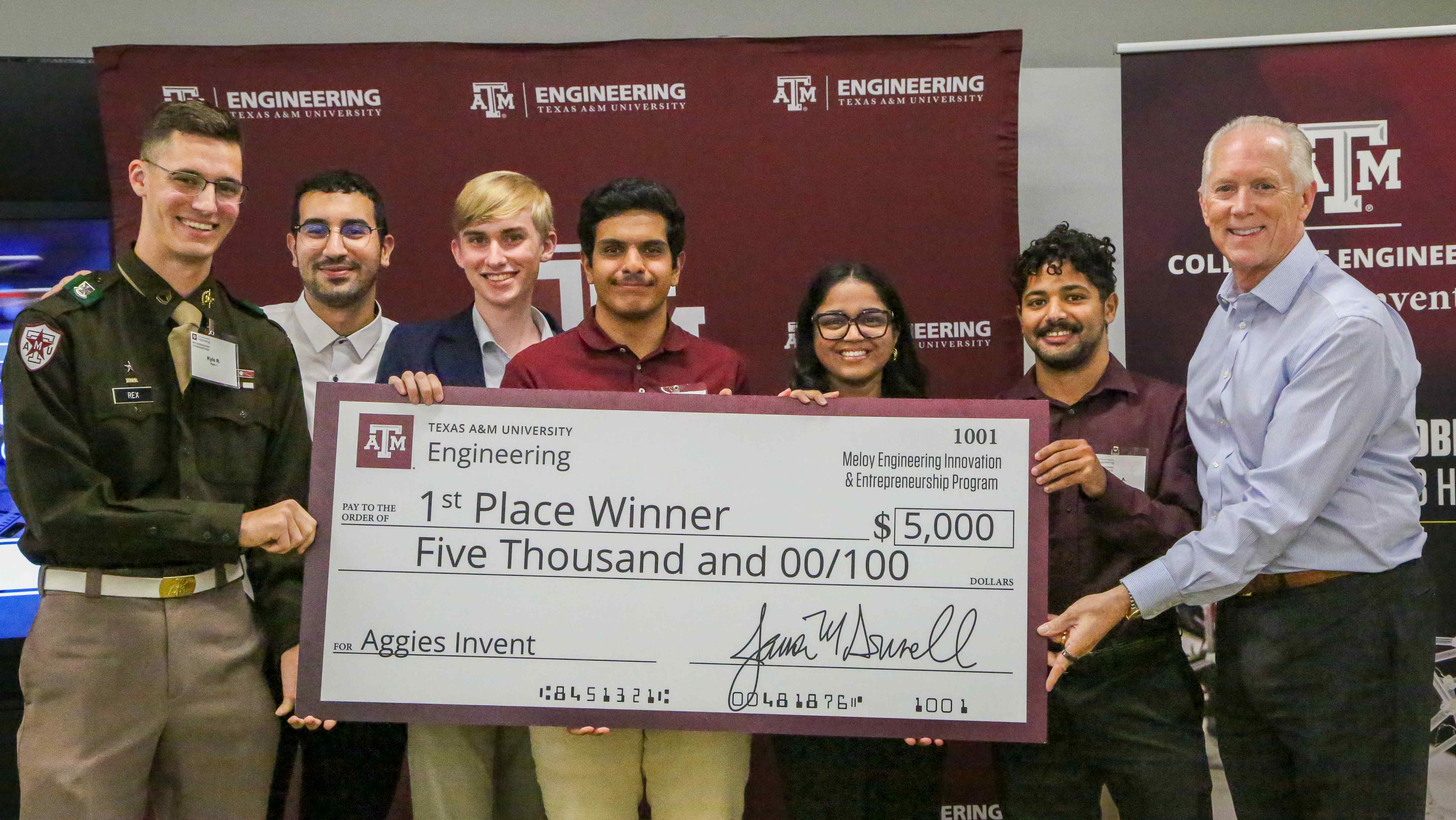 Six students and the director hold a large check for $5,000.