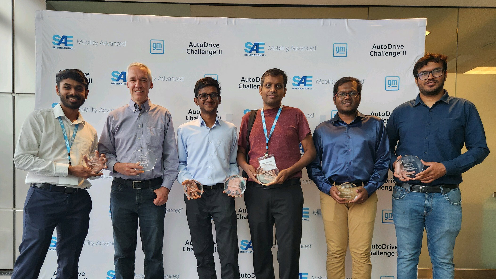 A group of six individuals posing with awards in front of a backdrop with the SAE and AutoDrive Challenge logos.