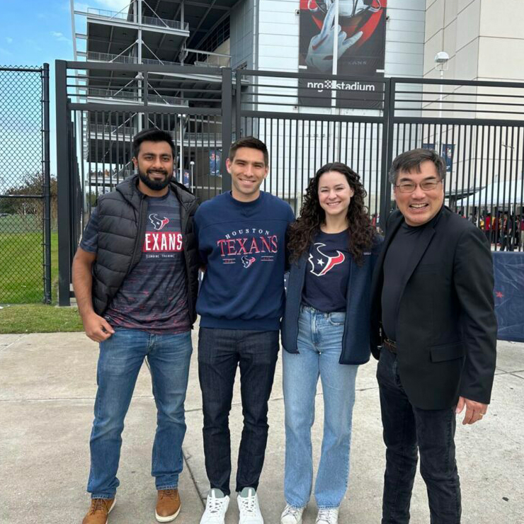 Four individuals smiling in front of a stadium, three wearing Houston Texans apparel.