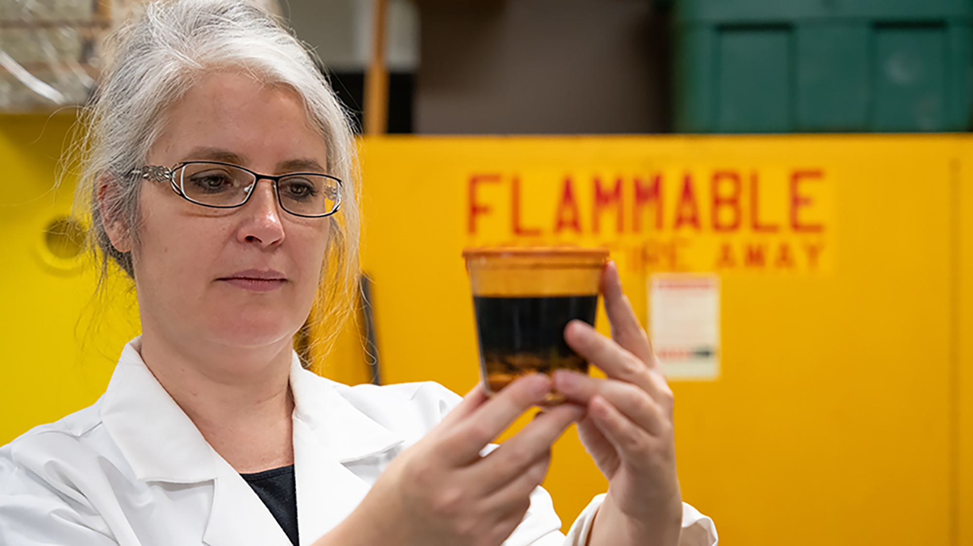 A womman looks at beaker of oil in laboratory.