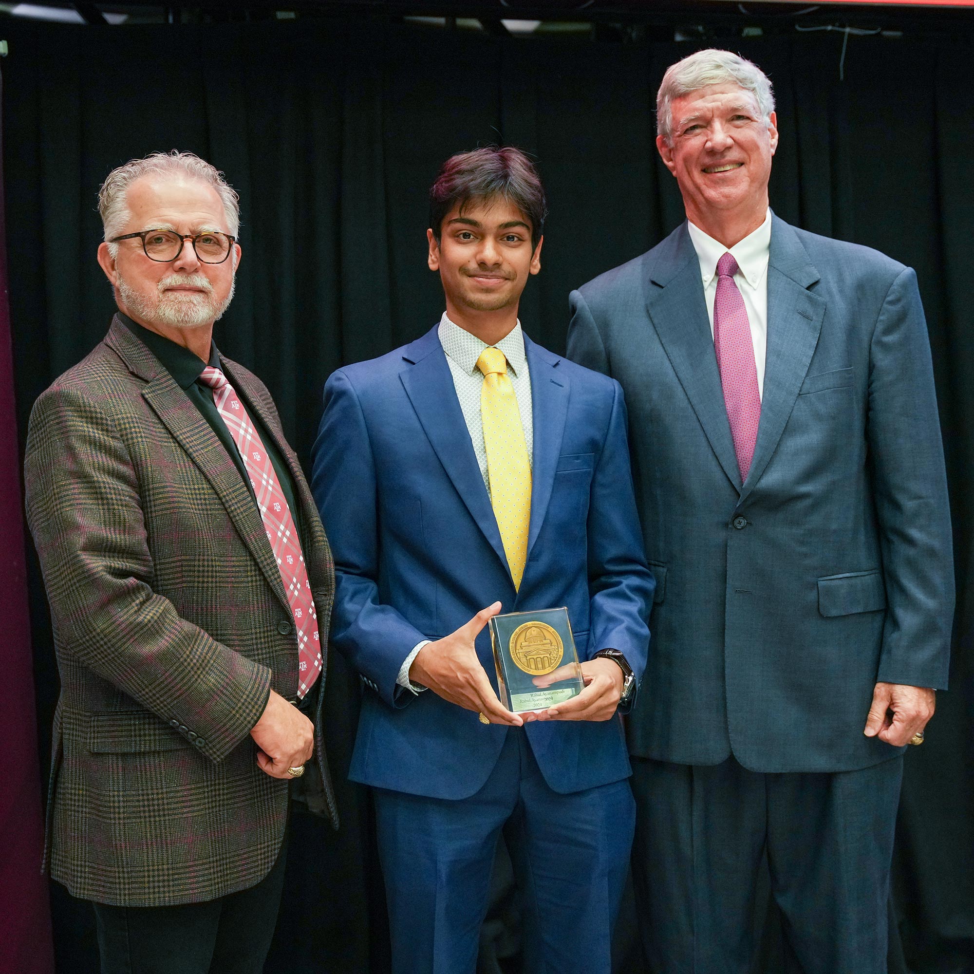 Three men standing, one with an award.