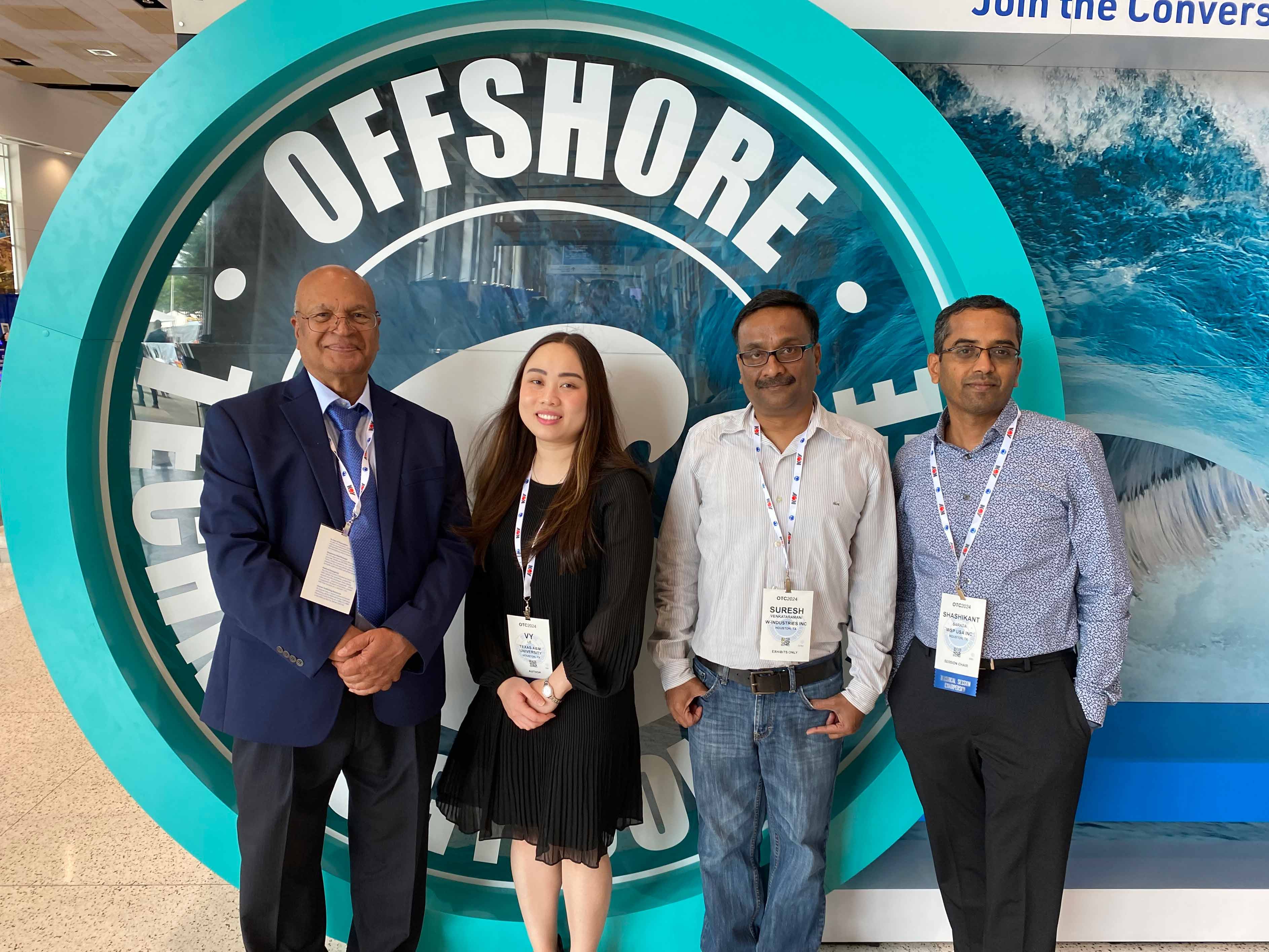 Four professionals wearing conference badges standing in front of a sign.