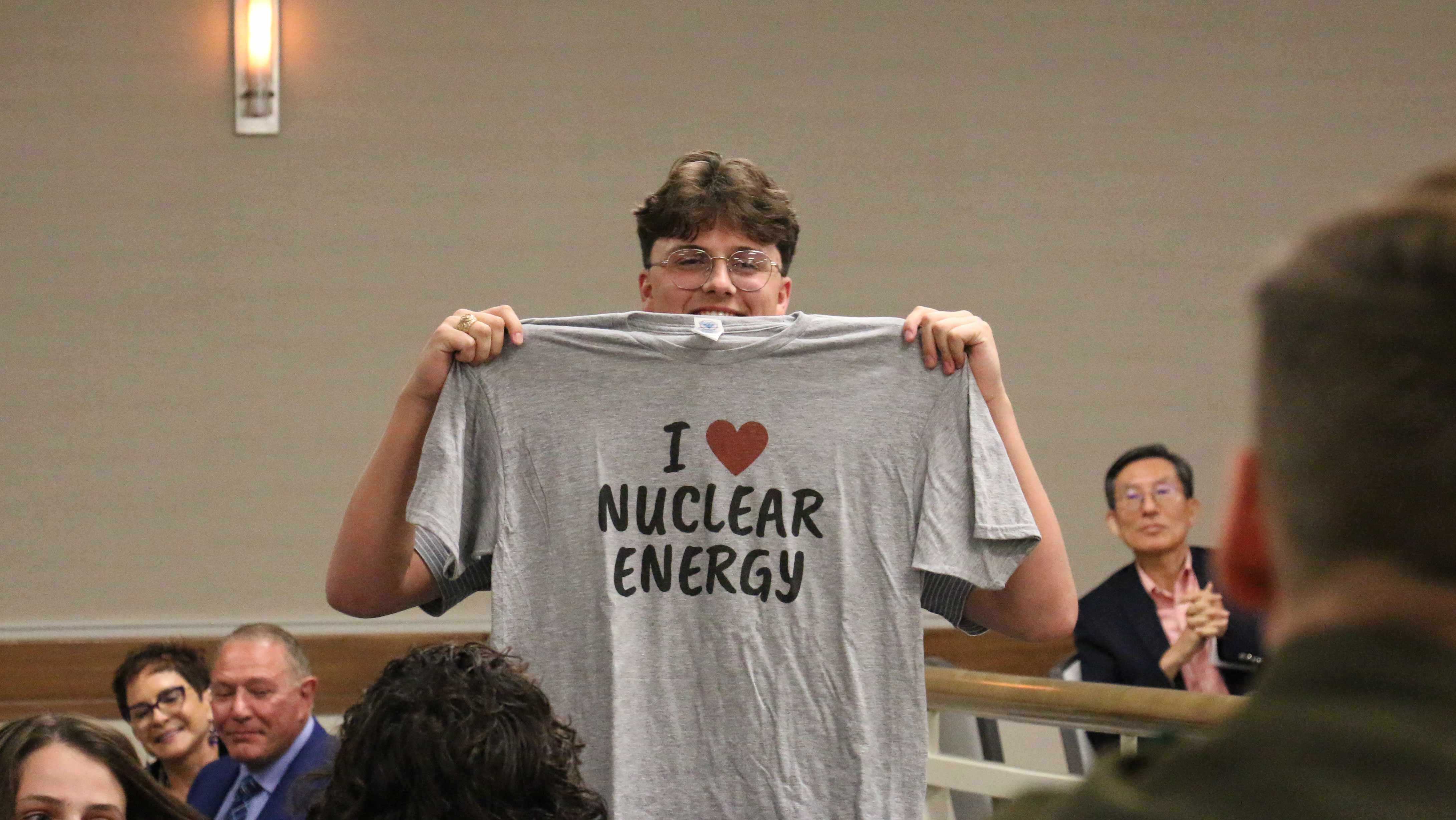 A man holds up a t-shirt with the text I heart nuclear energy.