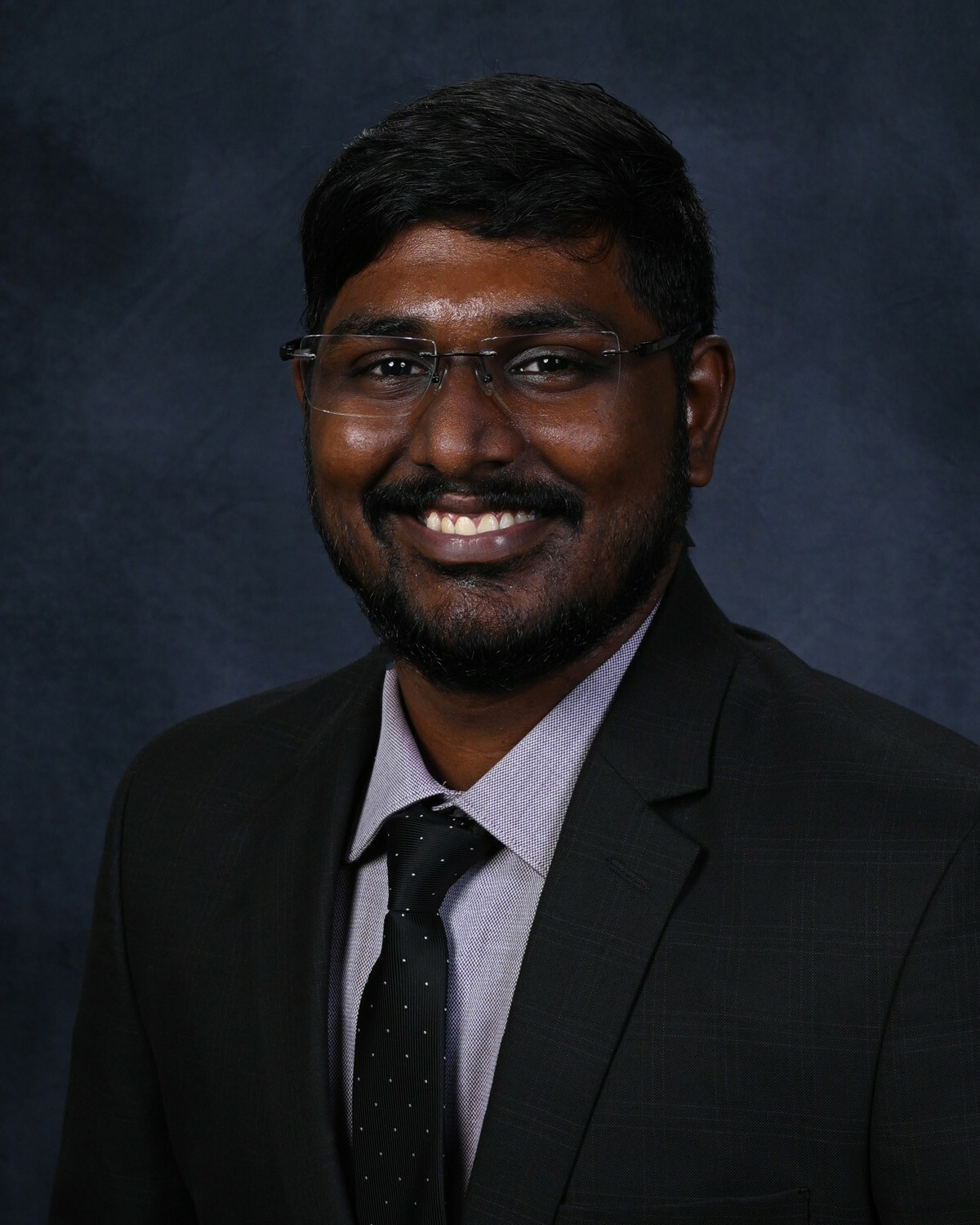 Headshot of man in dark suit with glasses. 