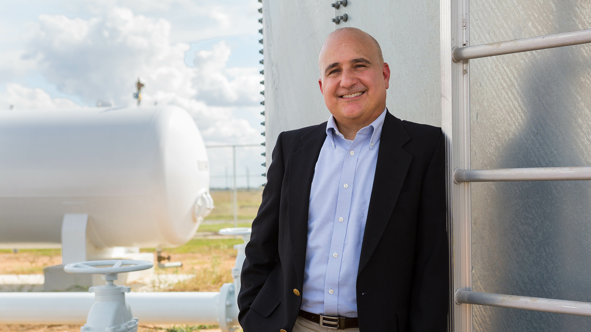 A man in a suit standing outside of a chemical plant.