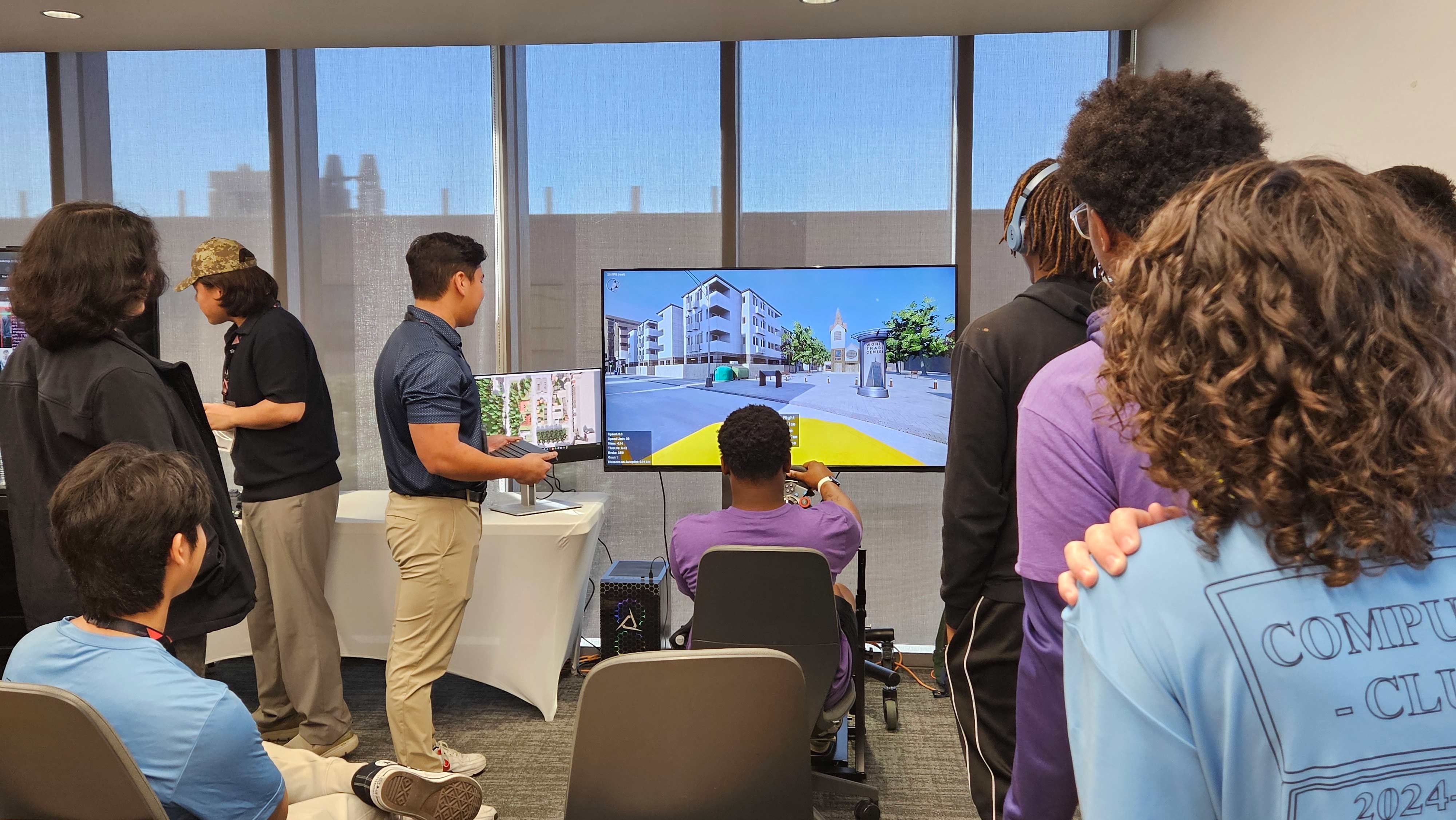 Student drives a car in a simulation as other people watch.