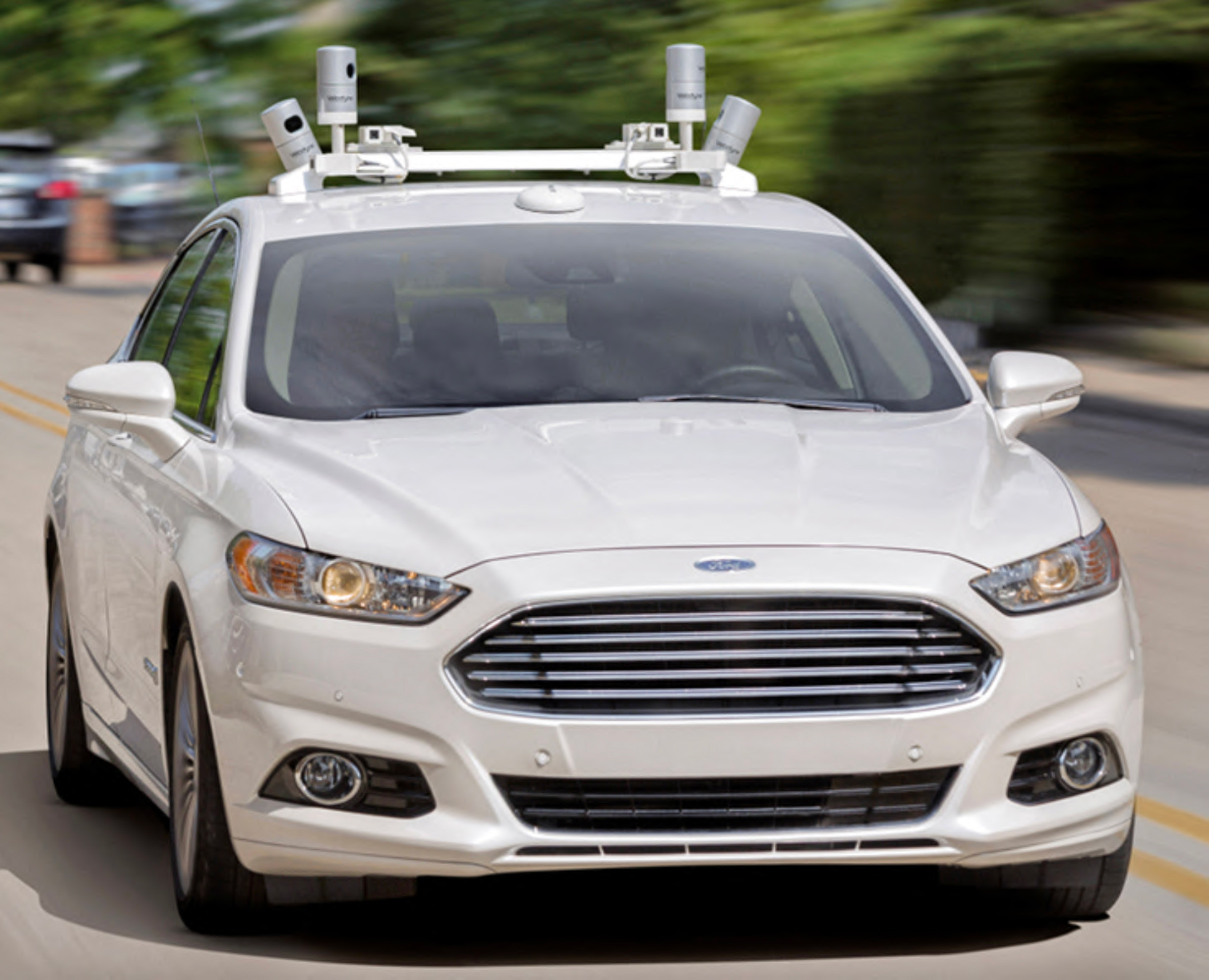 A white vehicle with cameras and sensors on its roof drives on a street.