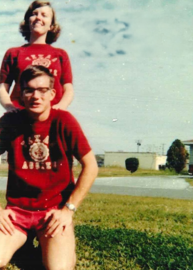 Young smiling woman standing behind a young man who’s kneeling.