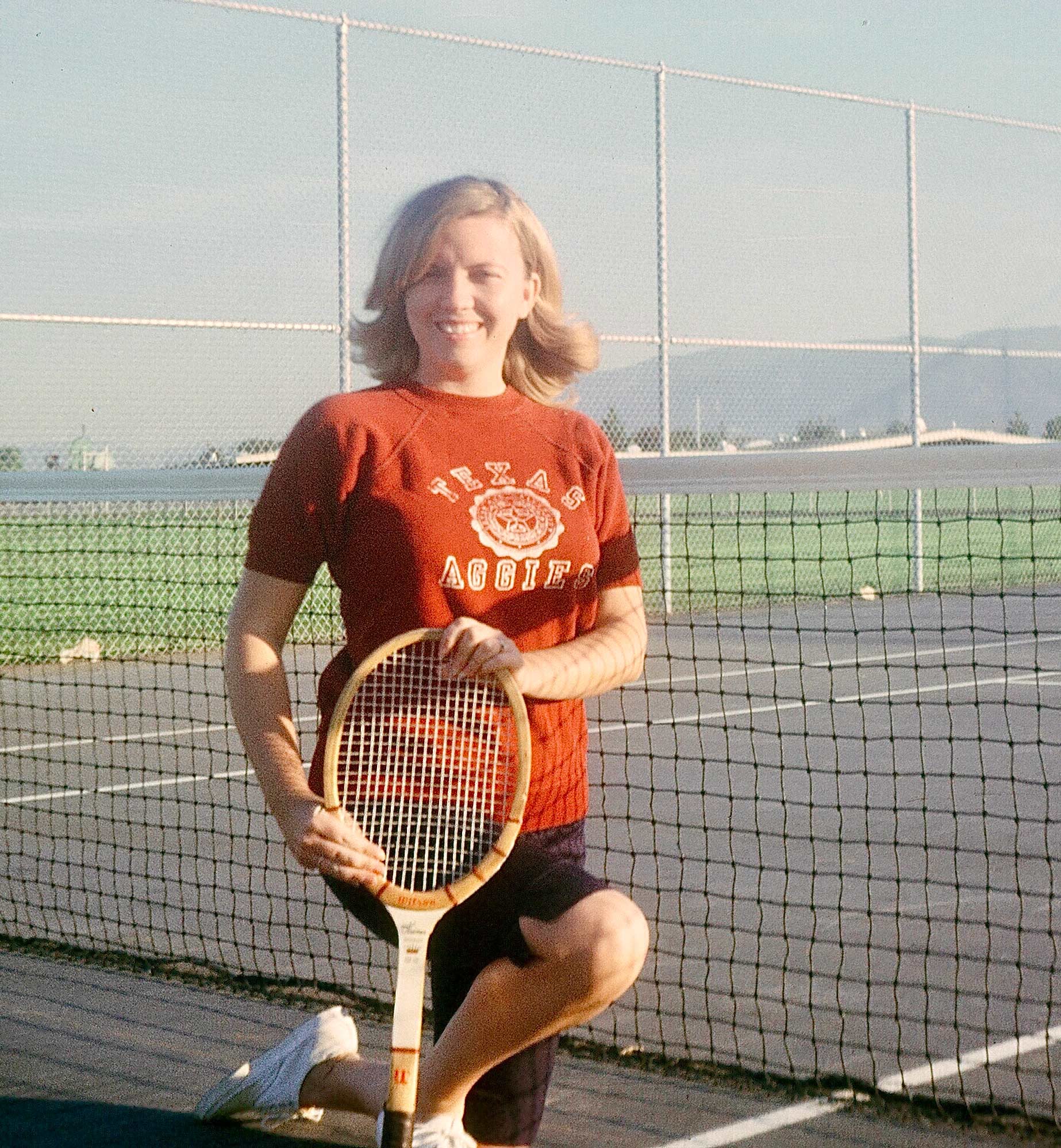 A woman posing with a tennis racket.