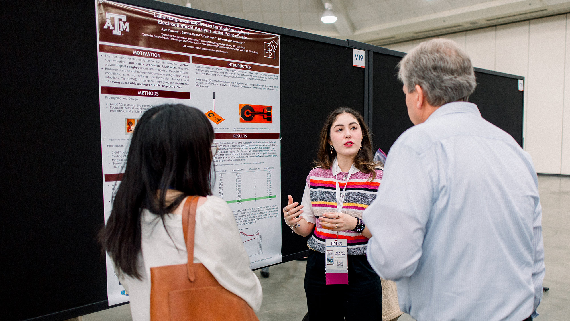 A person talking to two people by a research poster in a conference hall.