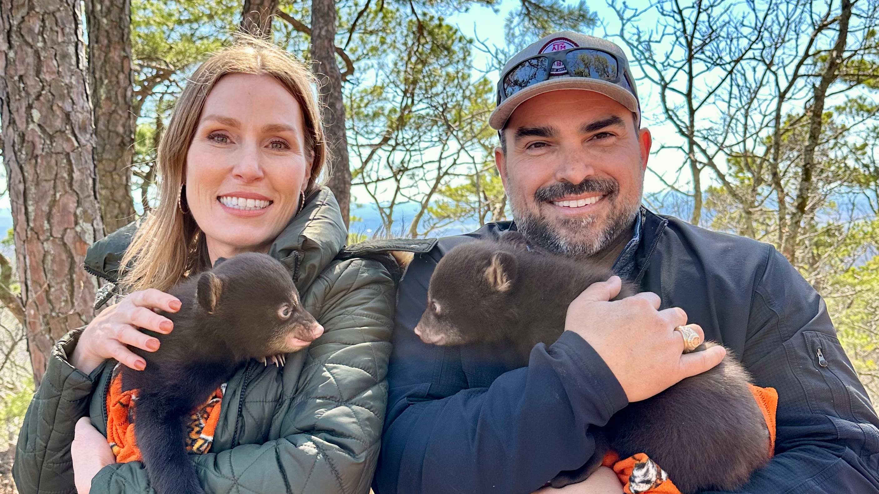 Man and woman holding bear cubs.