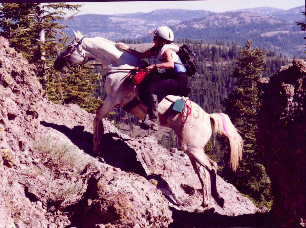 A woman riding a horse up a mountain.