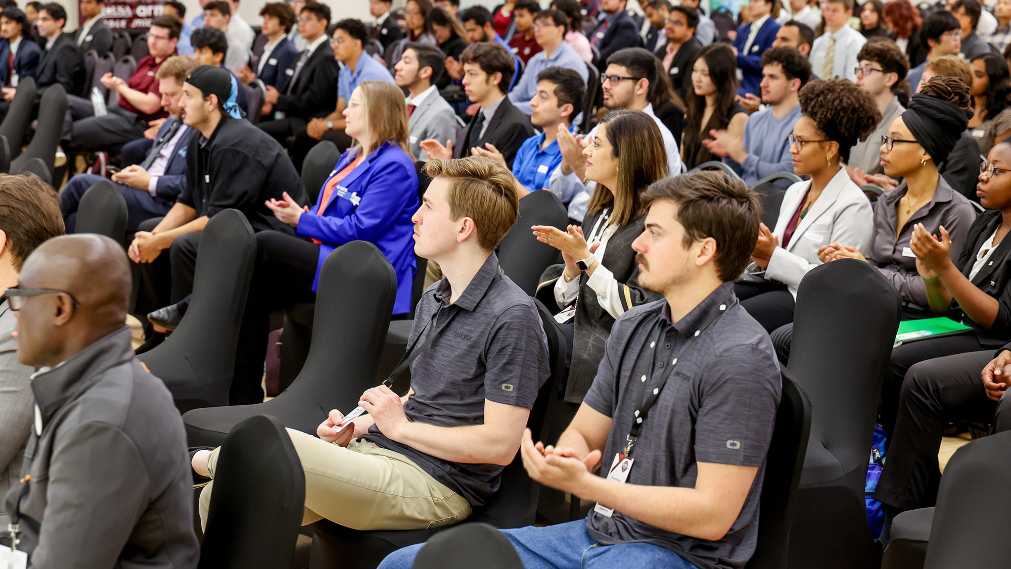 People seated in a large room, clapping.