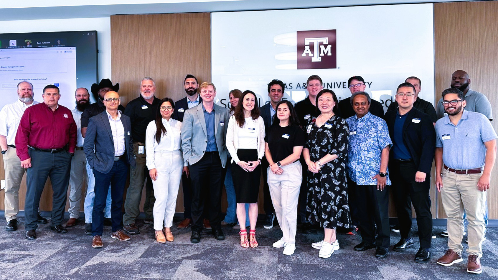 A large assembly standing in front of a Texas A&M University sign.