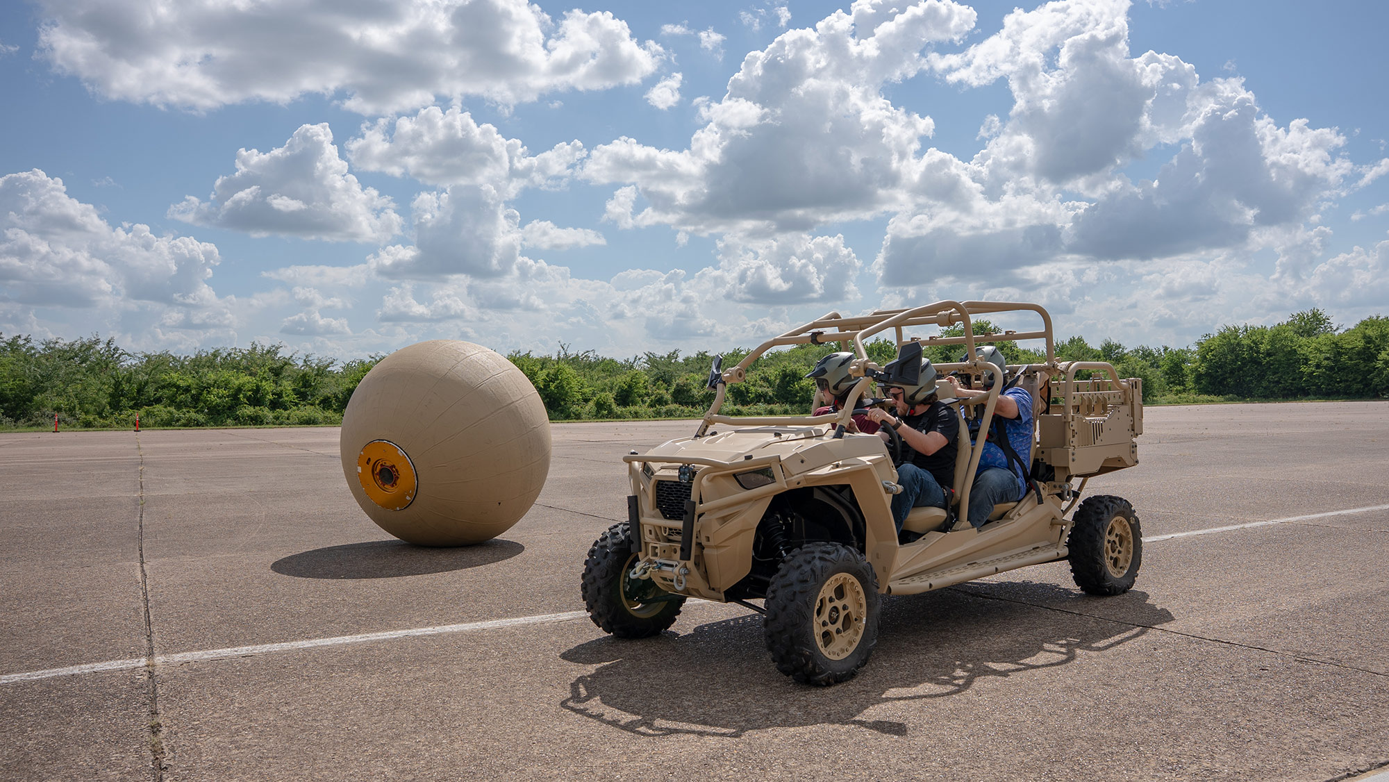  People riding in an all-terrain buggy next to a large ball. 