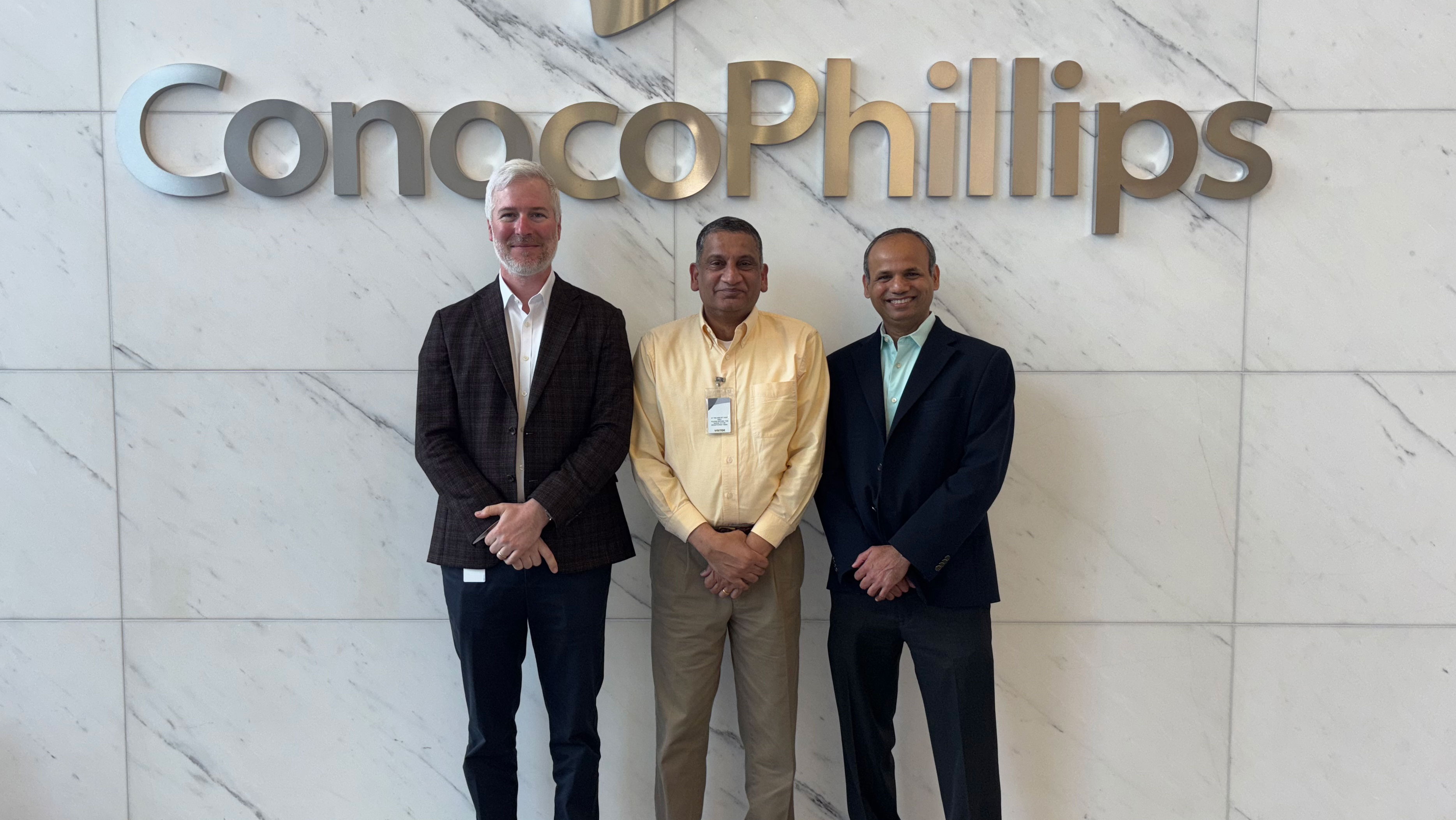 Three men stand in front of a ConocoPhillips sign.