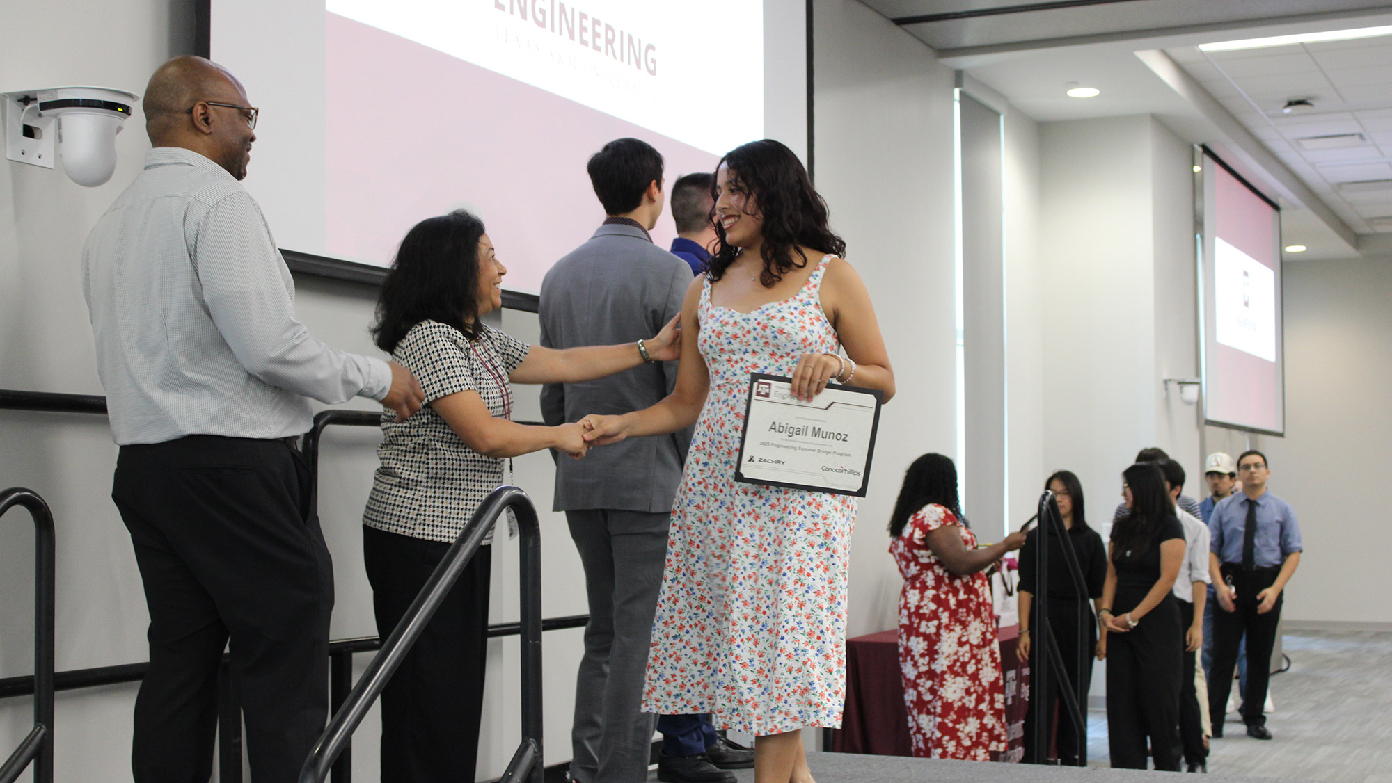 A group of students pose in front of a Texas A&M Engineering backdrop while holding certificates.