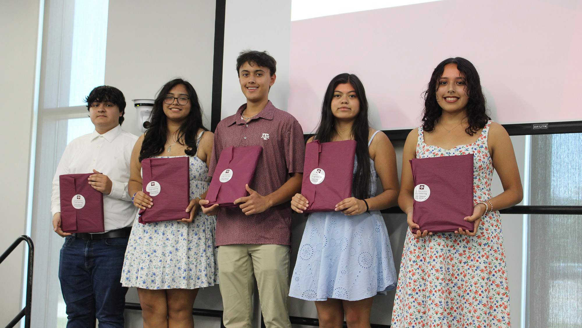 Five students stand in a row holding maroon wrapped gift on stage at the Summer Bridge Program ceremony.