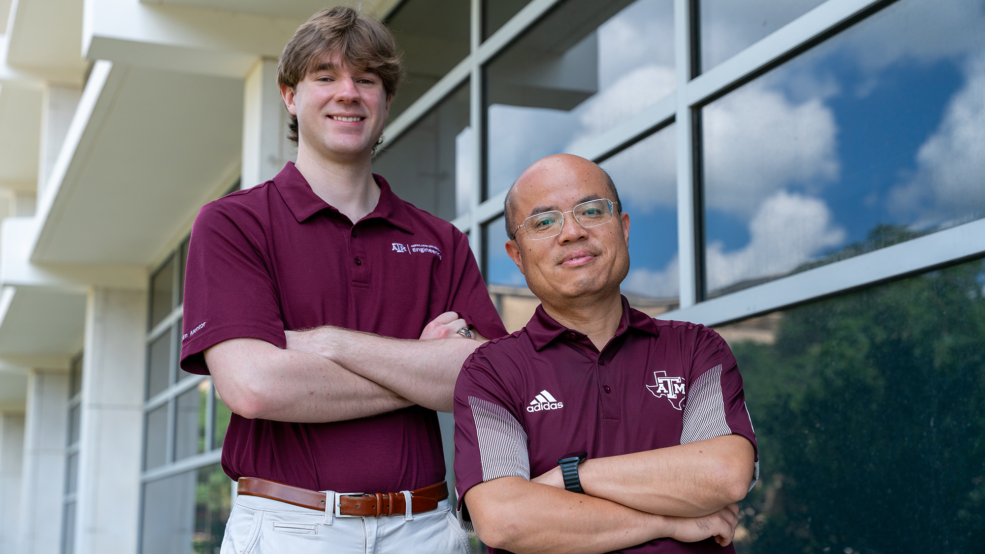 Two people standing with their arms crossed and smiling in front of a building.