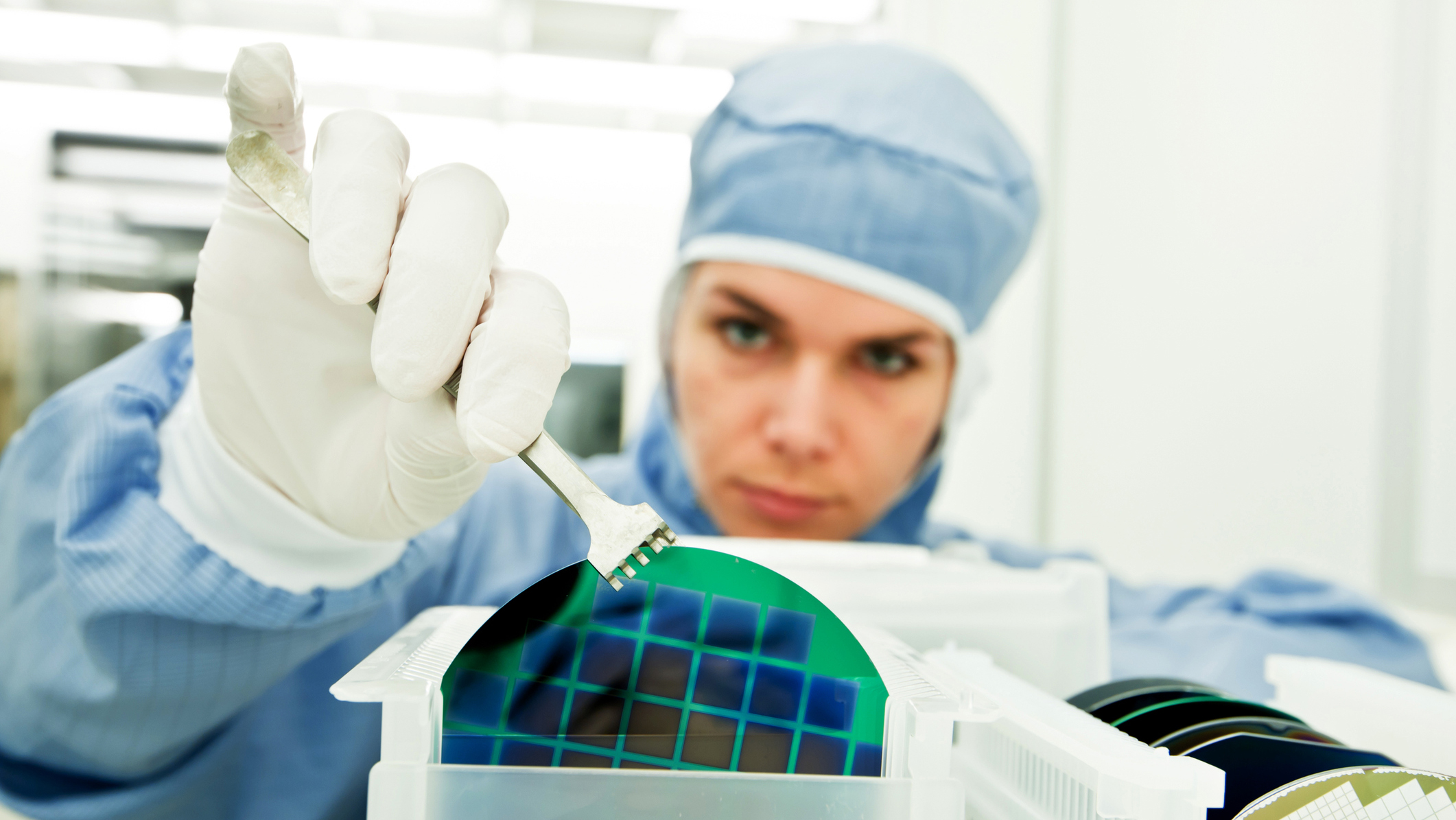 A woman in lab gear using a tool to pick up lab material.