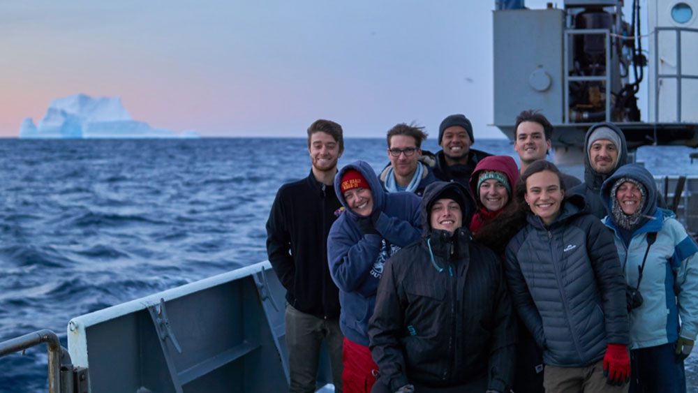 Some of the GO-SHIP Cruise crew pose with an iceberg in the background of their ship