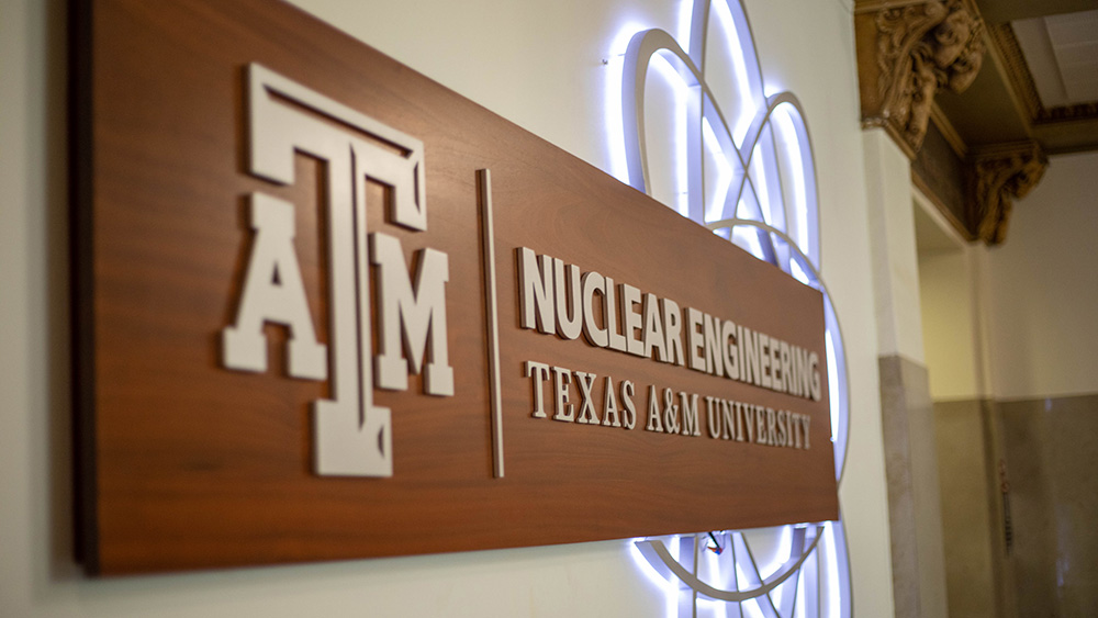 Wood sign with letters reading "Nuclear Engineering Texas A&amp;M University" with light up atom 