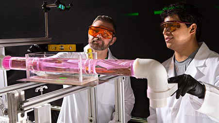 Two nuclear scientists in lab coats look at an experiment. 