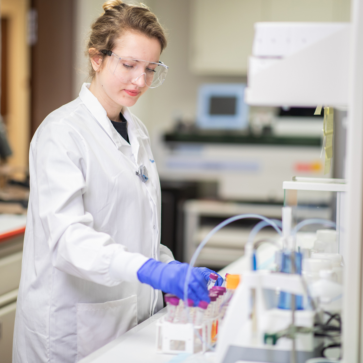 female student in protective lab clothing holding a vial with liquid in it