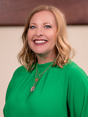 Jennifer House wearing a green blouse and gold necklaces standing