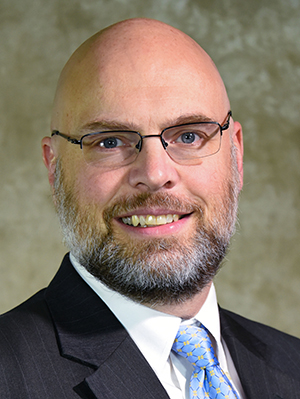 Dr. David Aumiller in suit in front of brown abstract backdrop