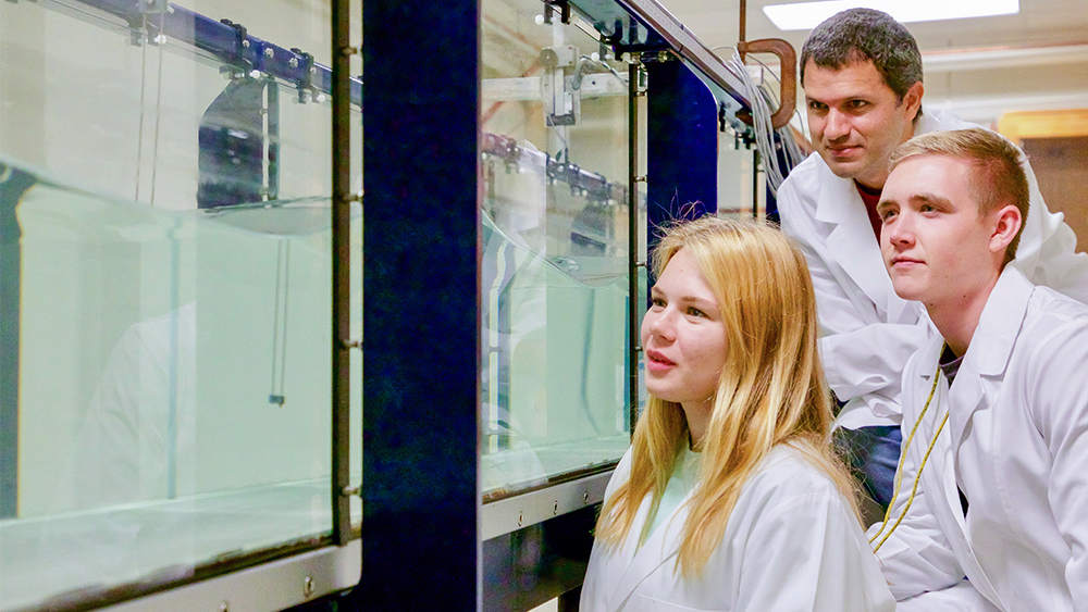 A professor and two students observe a wave tank simulation in the lab.