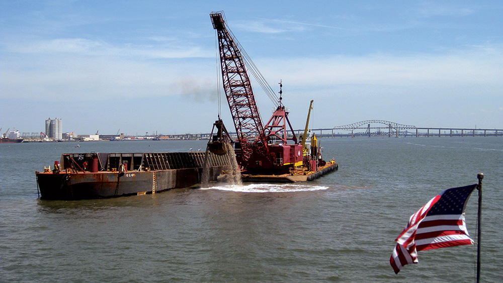Barge in water next to crane, American flag in foreground