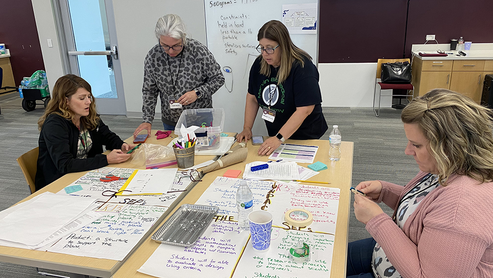 Educators sit around large tables writing in colorful markers on large pieces of paper. 