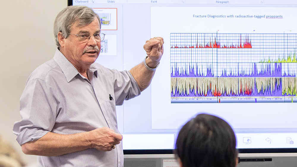 Male professor pointing out information on a classroom screen while standing in front of several seated petroleum engineering students