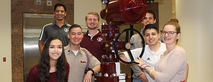 several Harold Vance Department of Petroleum Engineering students smiling and standing around lobby valve tree