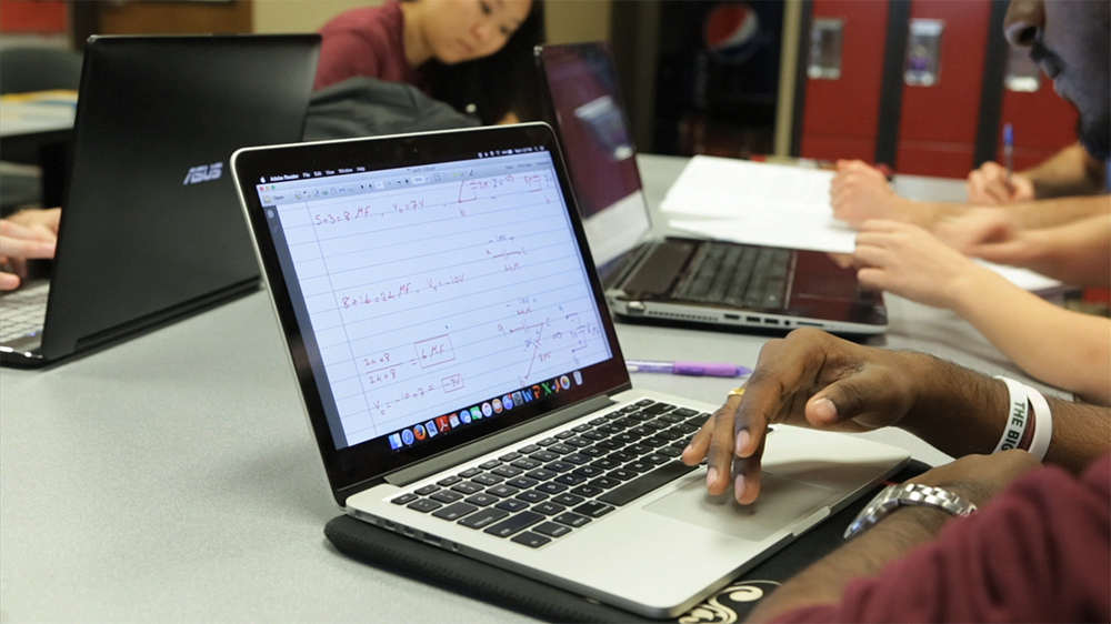 tabletop view of several petroleum engineering students' hands and their laptops