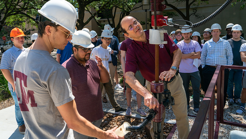 faculty member instructing undergraduate petroleum students outdoors near Aggie Well number one on Texas A&amp;M University campus